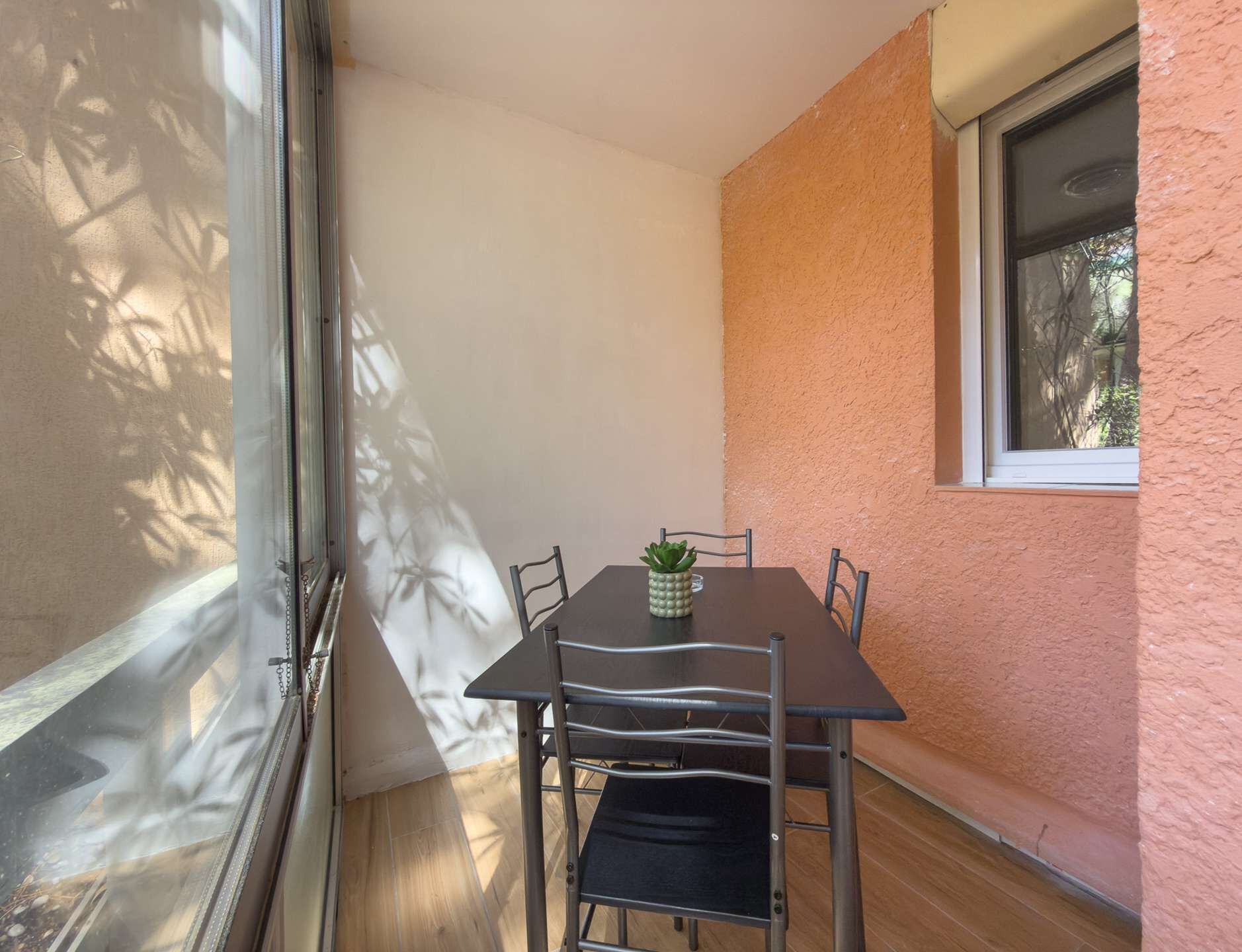 A corner room with a table and chairs, a window, and a plant on the table.