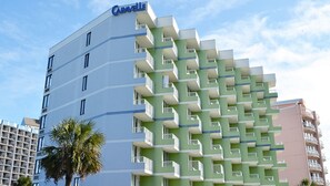 Un hotel de varios pisos con una fachada distintiva verde y blanca, balcones y una palmera en primer plano.