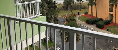 Un balcón con vista a la playa y al océano, un estacionamiento y un edificio de fachada verde y amarilla.