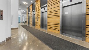 Een modern liftgedeelte met metalen en houten lambrisering, een gepolijste vloer en een duidelijk zichtbare noodknop.