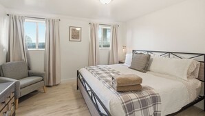 Ein Schlafzimmer mit einem Bett, einem Sessel, einem Nachttisch und einem Fenster.