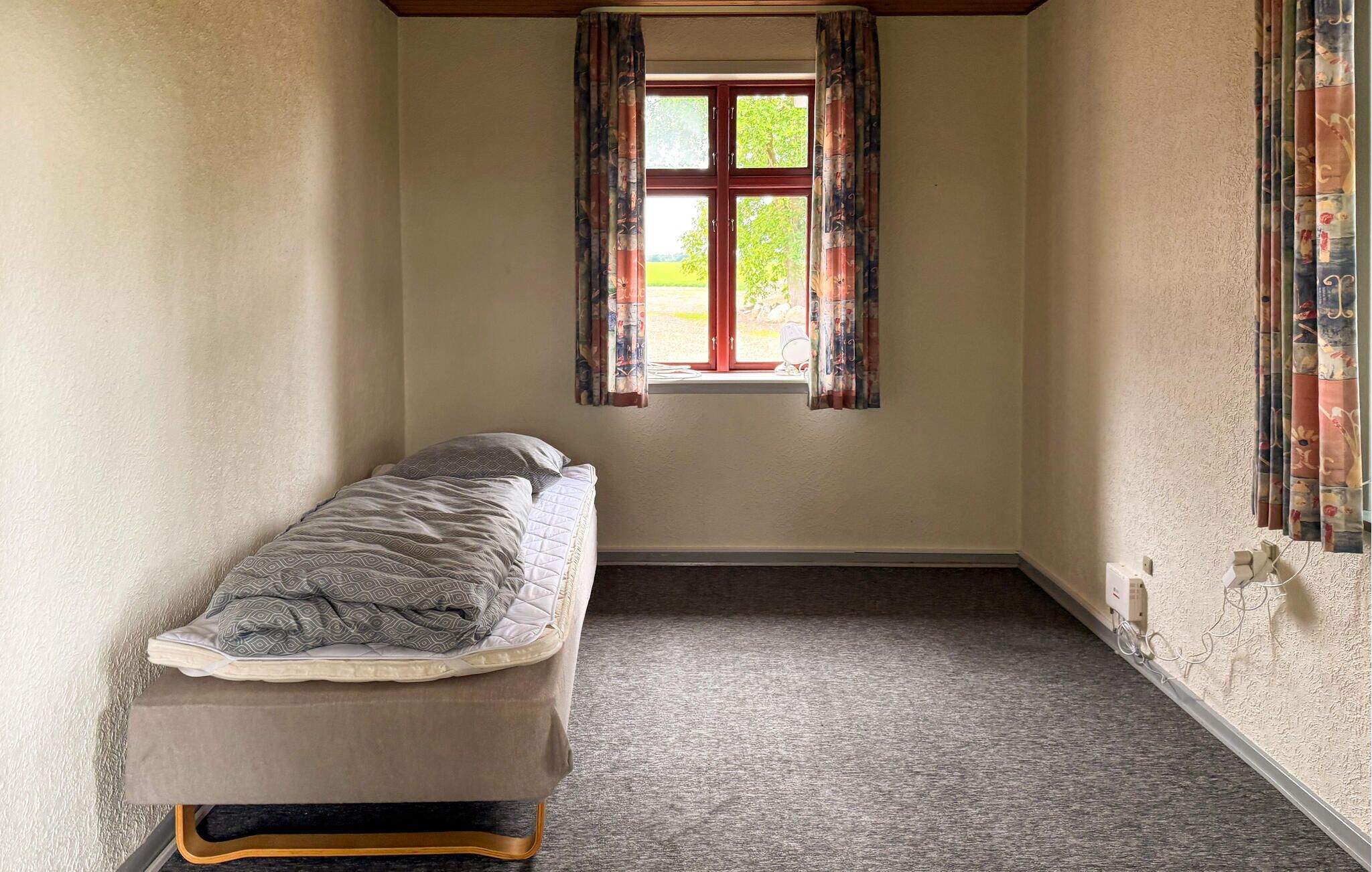 A narrow room with a single bed, a window with curtains, and a radiator on the wall.