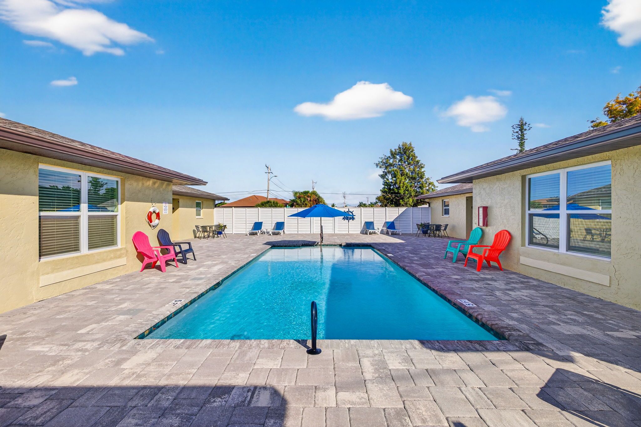 Et rektangulært swimmingpool med et sort sikkerhedsgelænder, omgivet af en belagt terrasse med liggestole og parasoller.
