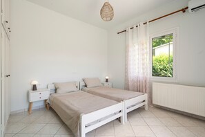 A bedroom with two beds, a window with curtains, a radiator, and a hanging light fixture.