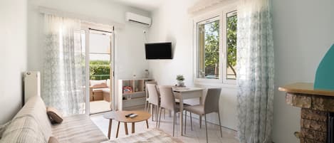 Een woonkamer met een bank, een eettafel met stoelen, een aan de muur bevestigde televisie en een raam met gordijnen.