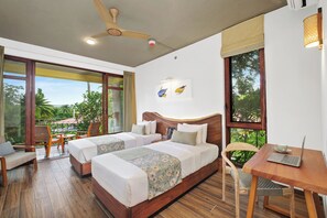Ein Hotelzimmer mit zwei Betten, einem Schreibtisch, einem Stuhl und einem Deckenventilator.