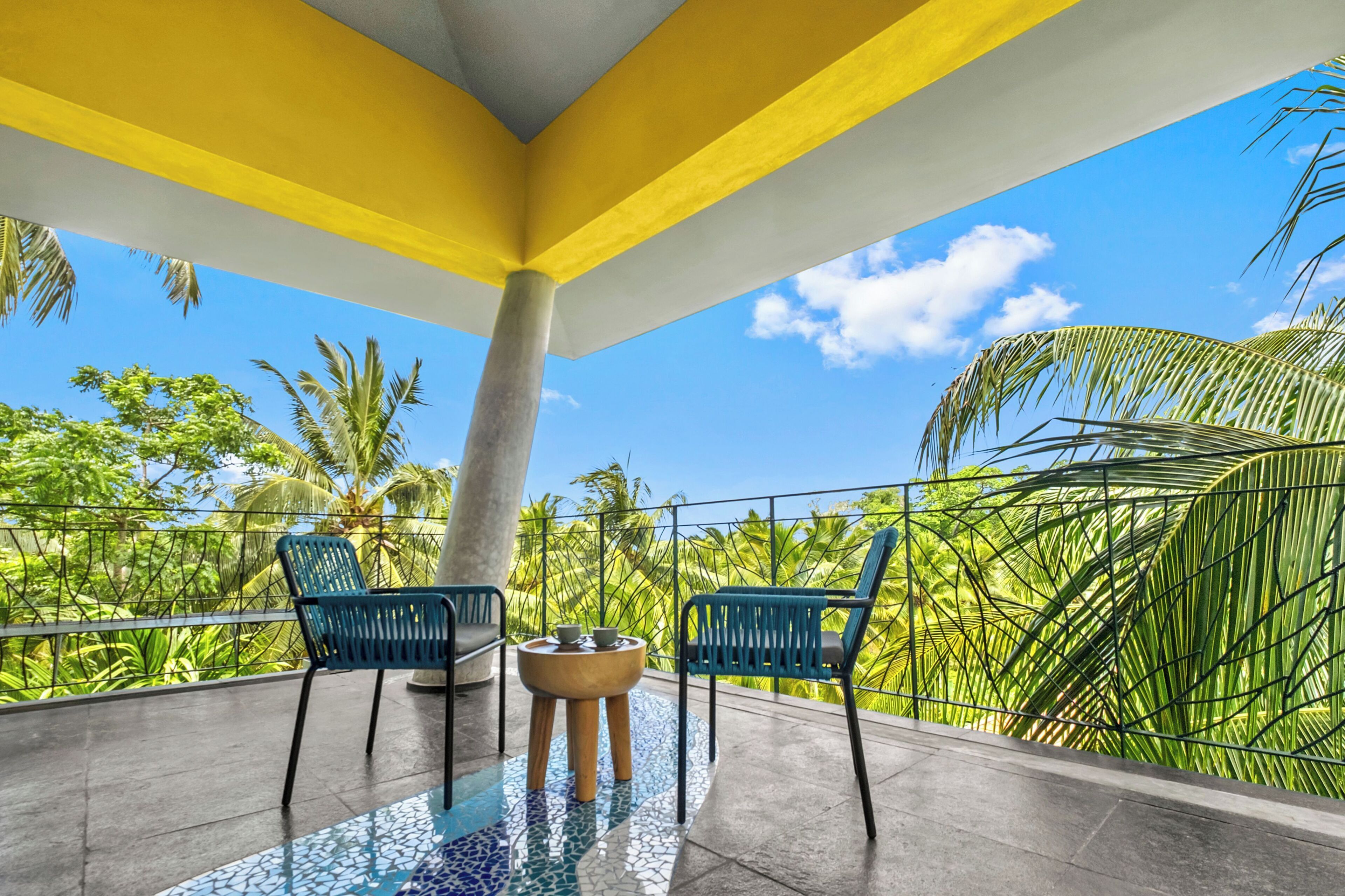 A balcony with two chairs, a small table, and a view of palm trees and clear sky.