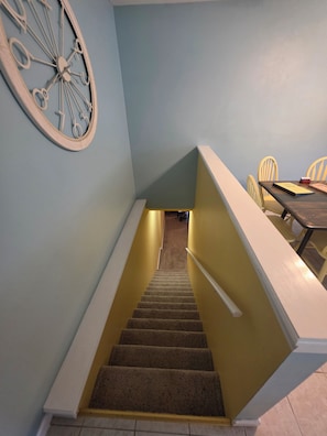 A staircase with carpeted steps leading to a landing, a dining table with chairs, and a wall clock. - Lakefront Cove Retreat, Private Dock, Huge Deck (Rocky Mount)