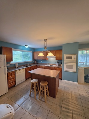 A kitchen with wooden cabinets, a central island with stools, a built-in microwave, and a refrigerator. - Lakefront Cove Retreat, Private Dock, Huge Deck (Rocky Mount)