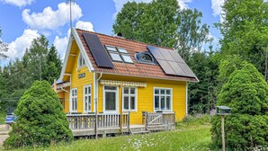 A yellow house with solar panels, a deck, and a sign reading 'HYLTA.'