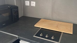 Cozinha com bancada preta, tábua de corte de madeira, forno embutido e armários brancos.