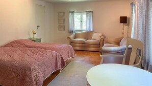 Une chambre à coucher comprenant un lit, une chaise, une table, une fenêtre avec des rideaux et des tableaux accrochés au mur.