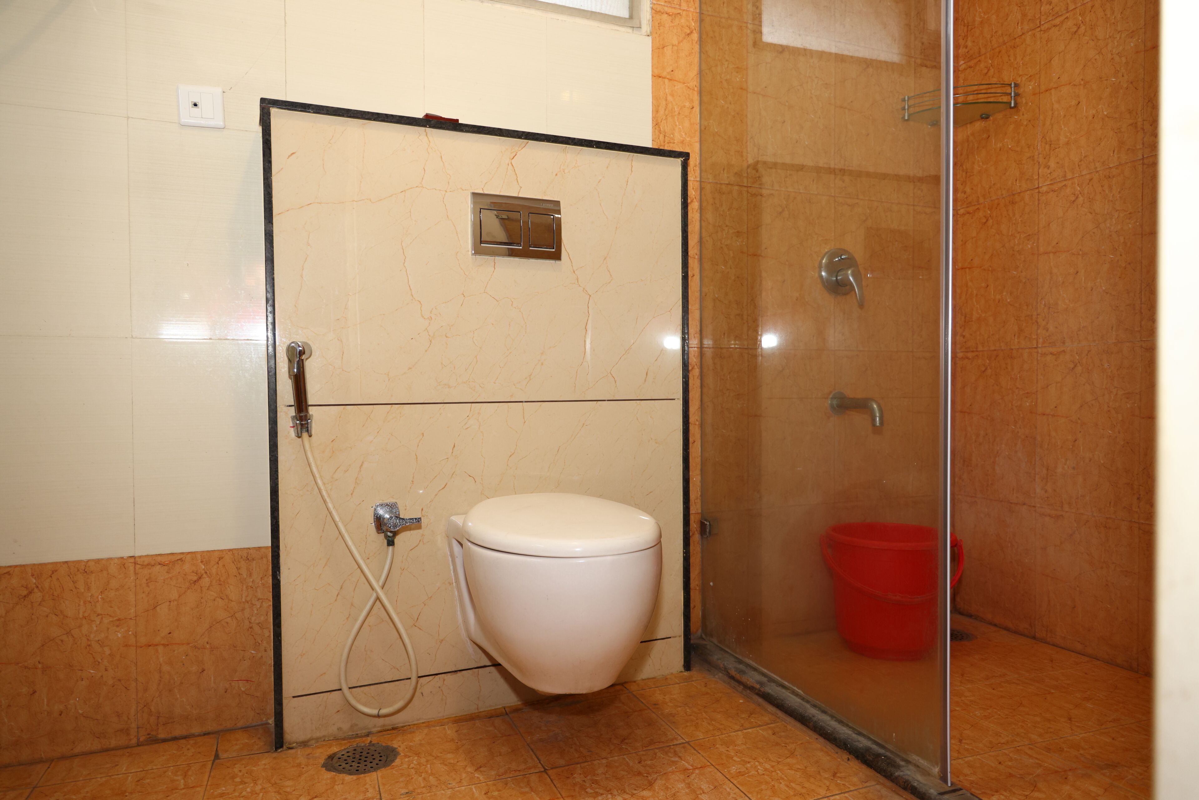 A bathroom with a toilet, shower, and a red bucket.