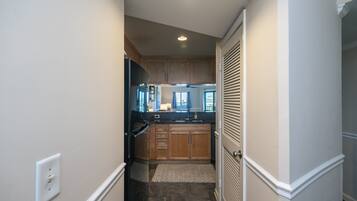 A narrow hallway leading to a kitchen with wooden cabinets, a black refrigerator, and a window with curtains.