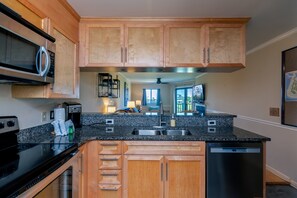 A modern kitchen with wooden cabinets, a granite countertop, stainless steel appliances, and a view into the dining area.