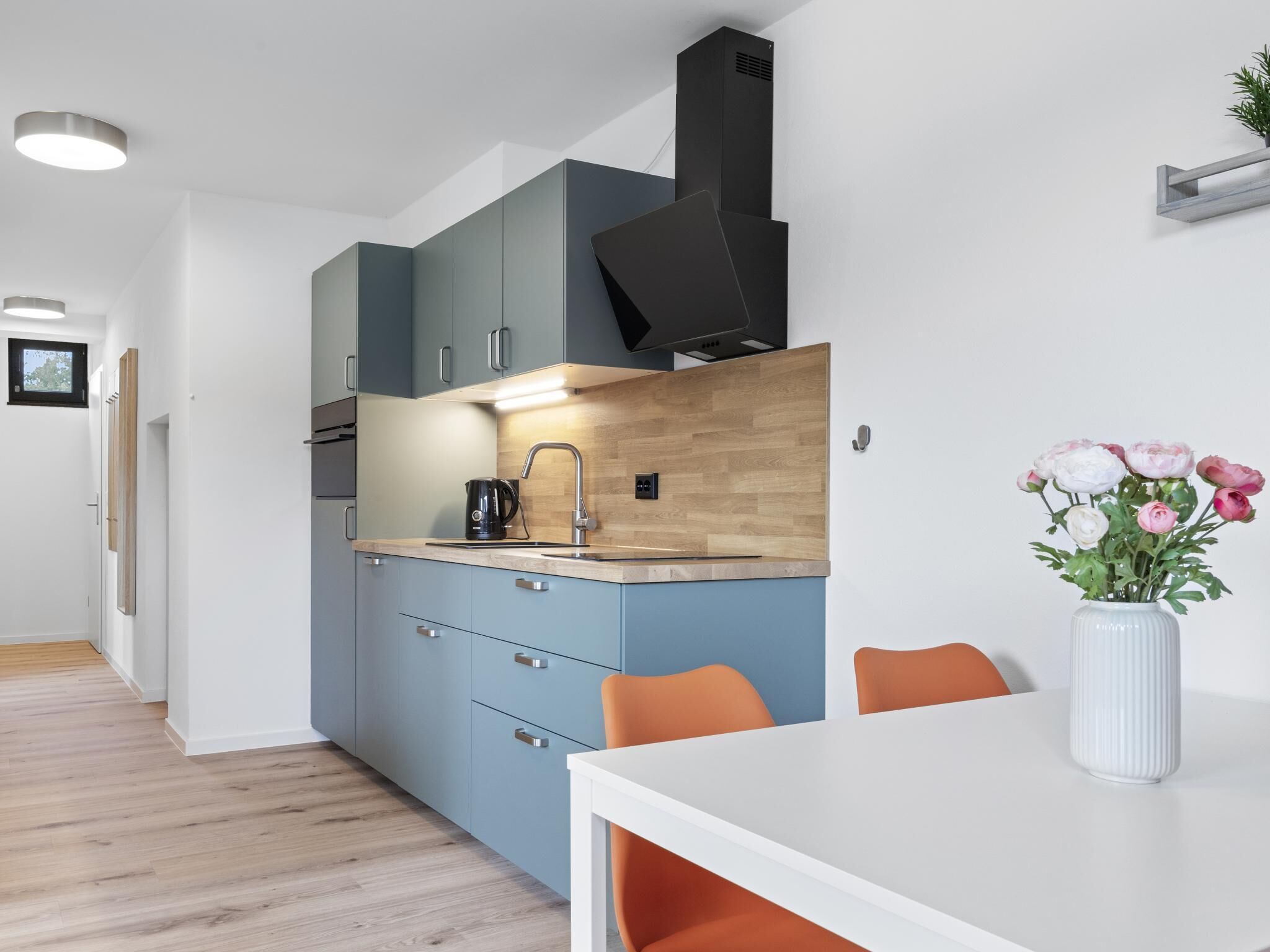 A modern kitchen with grey cabinets, a wooden countertop, and a black range hood.