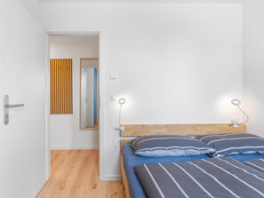 A bedroom with a wooden bed, two bedside lamps, a mirror, and a door leading to another room. - 2 Large Apartments by the Baltic Sea (Hohenkirchen OT Beckerwitz)