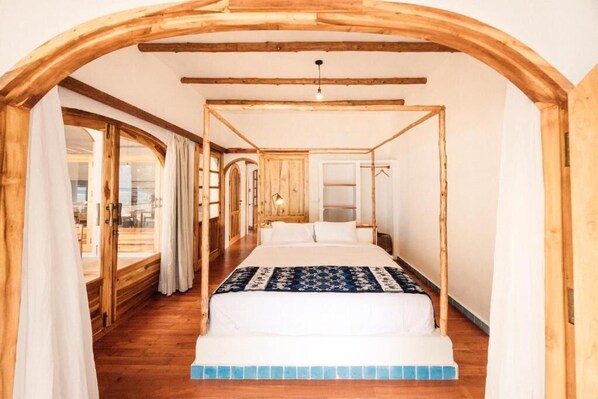 Ein Zimmer mit Himmelbett, Holzbalken, einem großen Fenster und Blick ins Freie.