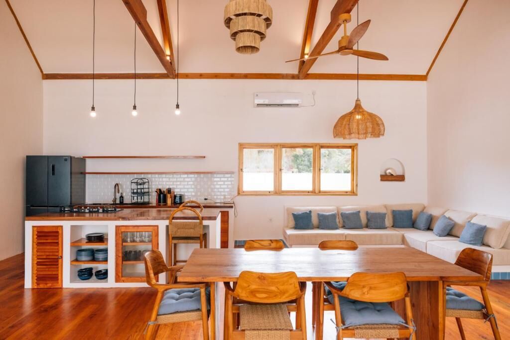 A modern kitchen with wooden cabinets, a dining area with a wooden table and chairs, and a large window providing natural light.