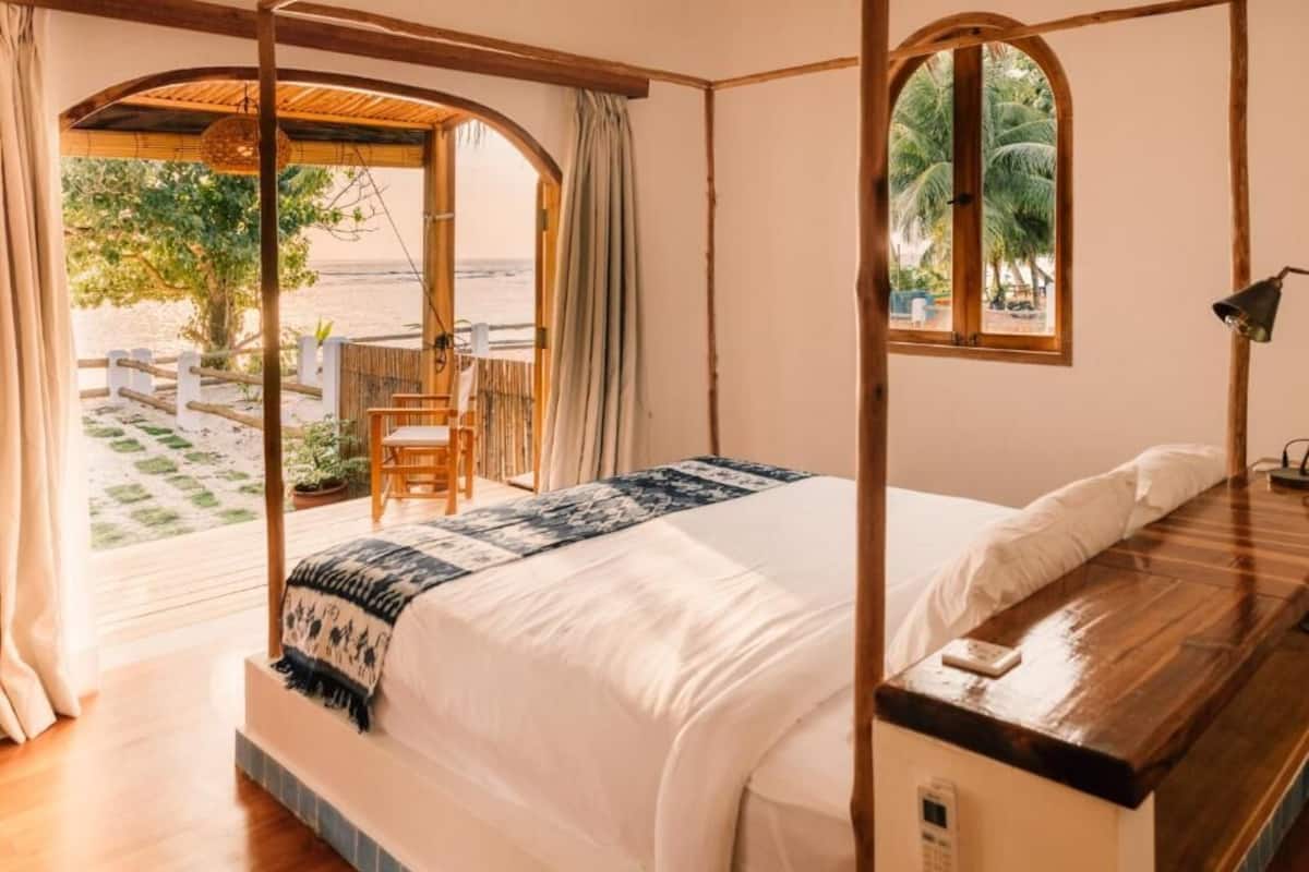 A bedroom with a bed, a window, and a view of the beach.