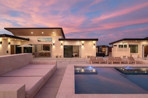 Ein modernes Haus mit Pool, Sitzgelegenheiten im Freien und einem Sonnenuntergangshimmel.