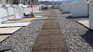A wooden boardwalk leading to beach huts with a rocky beach and buildings in the background.