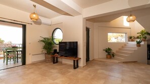 A spacious living area with a flat-screen TV on a wooden stand, a large mirror, and a staircase with potted plants. - Alice On The Rocks Villa with Sea View, Wi-Fi, and Air Conditioning (Vathianos Kampos)