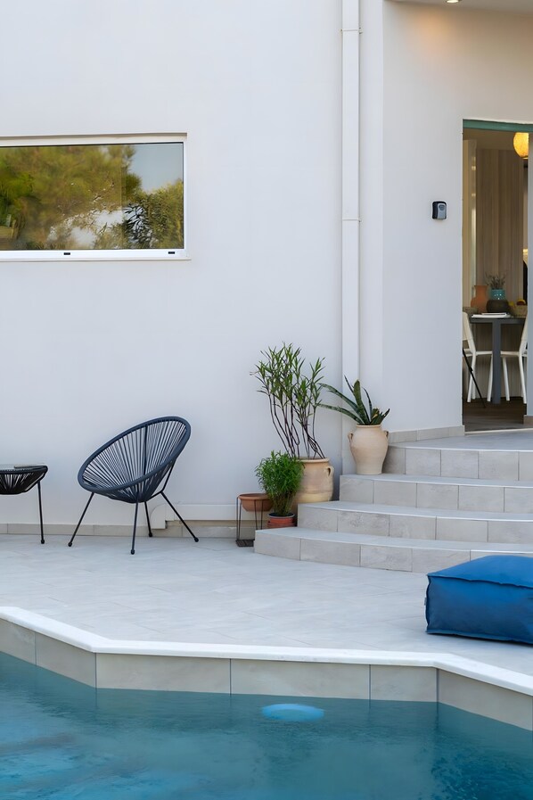 A modern outdoor pool area with a seating arrangement and potted plants.