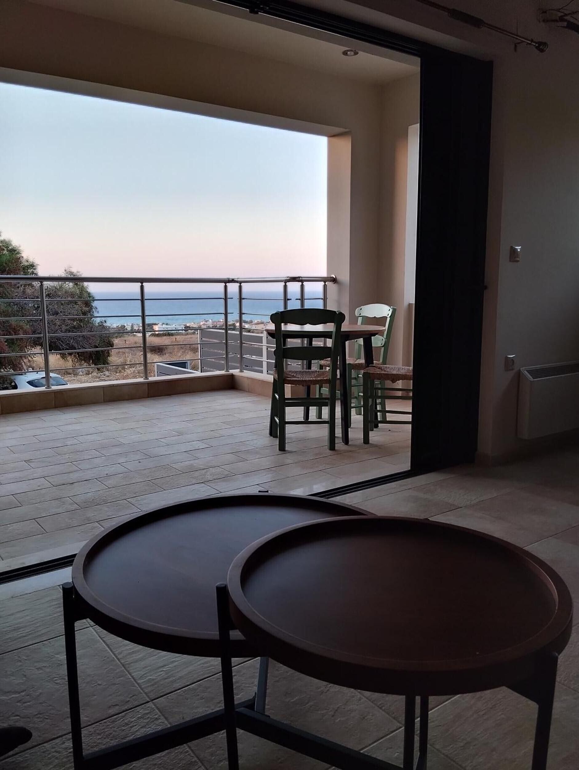 A balcony with a view of the sea, a table, and chairs.