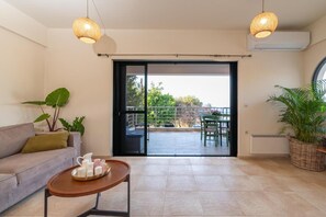 A living room with a sofa, a coffee table, and a balcony with a table and chairs. - Alice On The Rocks Villa with Sea View, Wi-Fi, and Air Conditioning (Vathianos Kampos)
