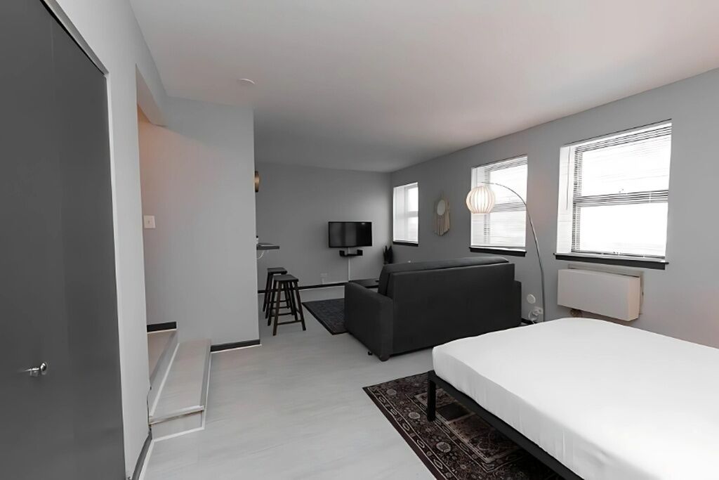 Ein modernes Hotelzimmer mit Bett, einer Couch, einem Fernseher und einer kleinen Küchenzeile.
