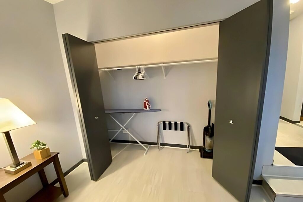 A compact room with a desk, chair, and a small table with a lamp.