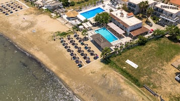 Vue aérienne d’un hôtel situé sur la côte, avec une piscine, des chaises longues sur la plage et une plage.