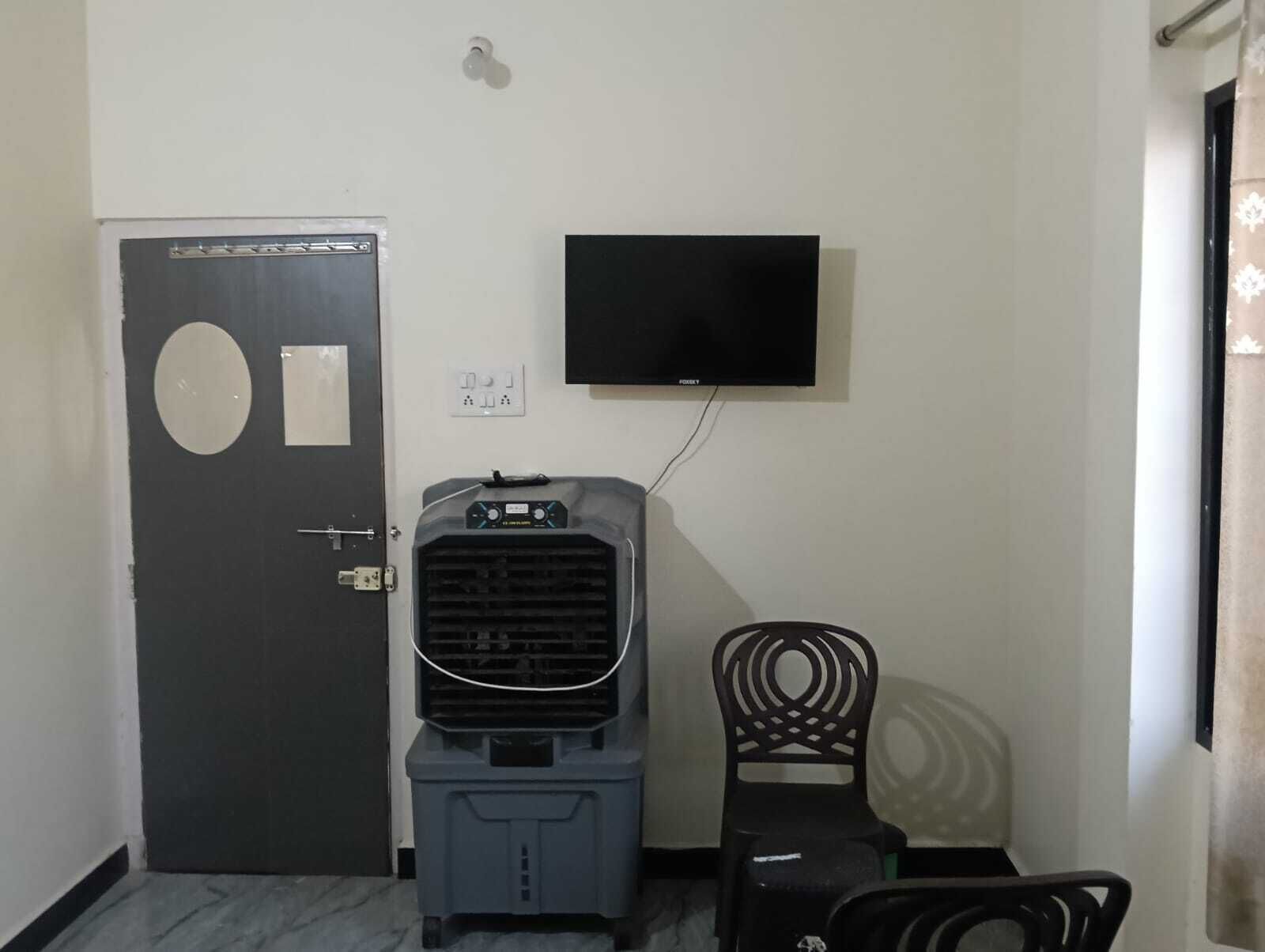 A room with a door, a television mounted on the wall, a water cooler, and a chair.