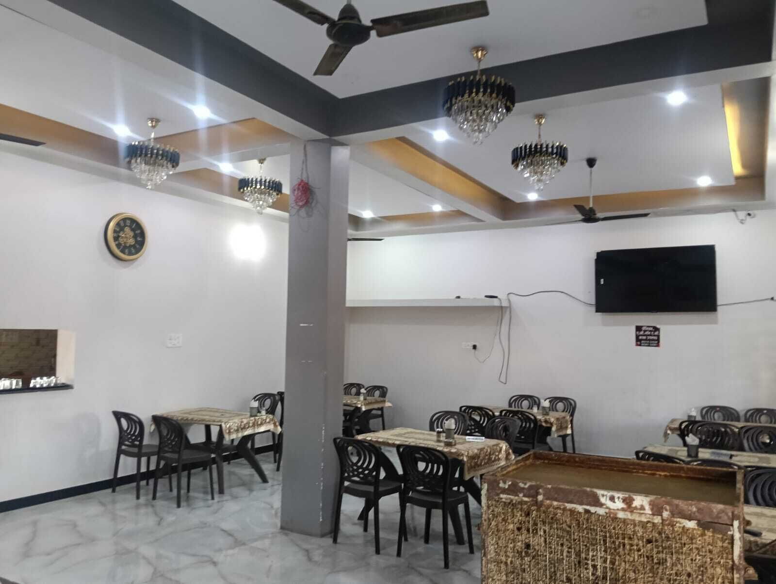 A dining area with tables, chairs, chandeliers, a clock, and a television on the wall.