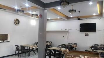 A dining area with tables, chairs, chandeliers, a clock, and a television on the wall.