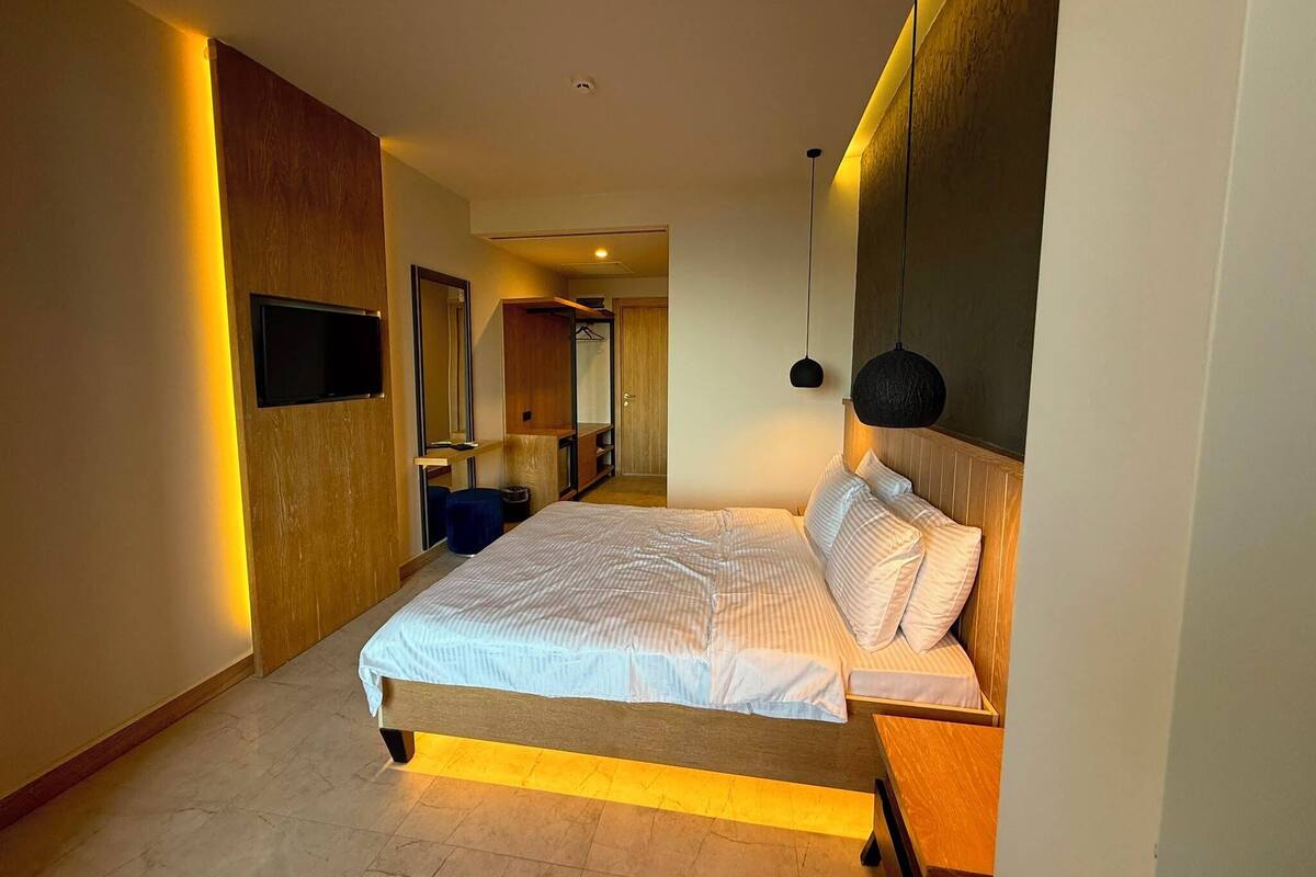 A modern hotel room with a large bed, bedside tables, a wardrobe, a mirror, and a television.