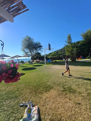 A grassy outdoor area with a basketball hoop, a picnic table, and a beach in the background. - Apartment 'Marina's Houses By The Sea - Apt 4' with Sea View, Wi-Fi and Air Conditioning (Kassandra)