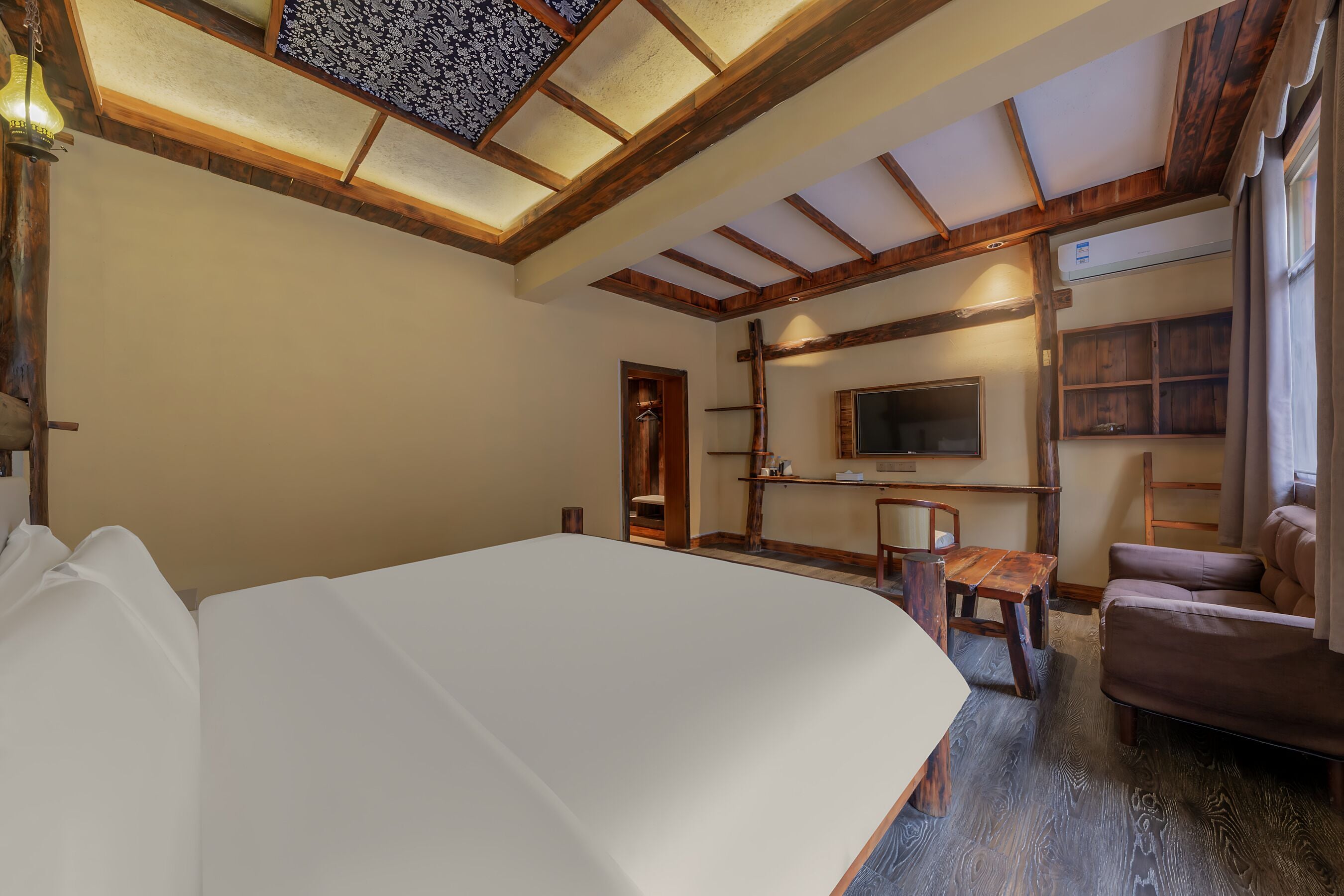 A bedroom with a large bed, wooden ceiling beams, a TV, and a small table.