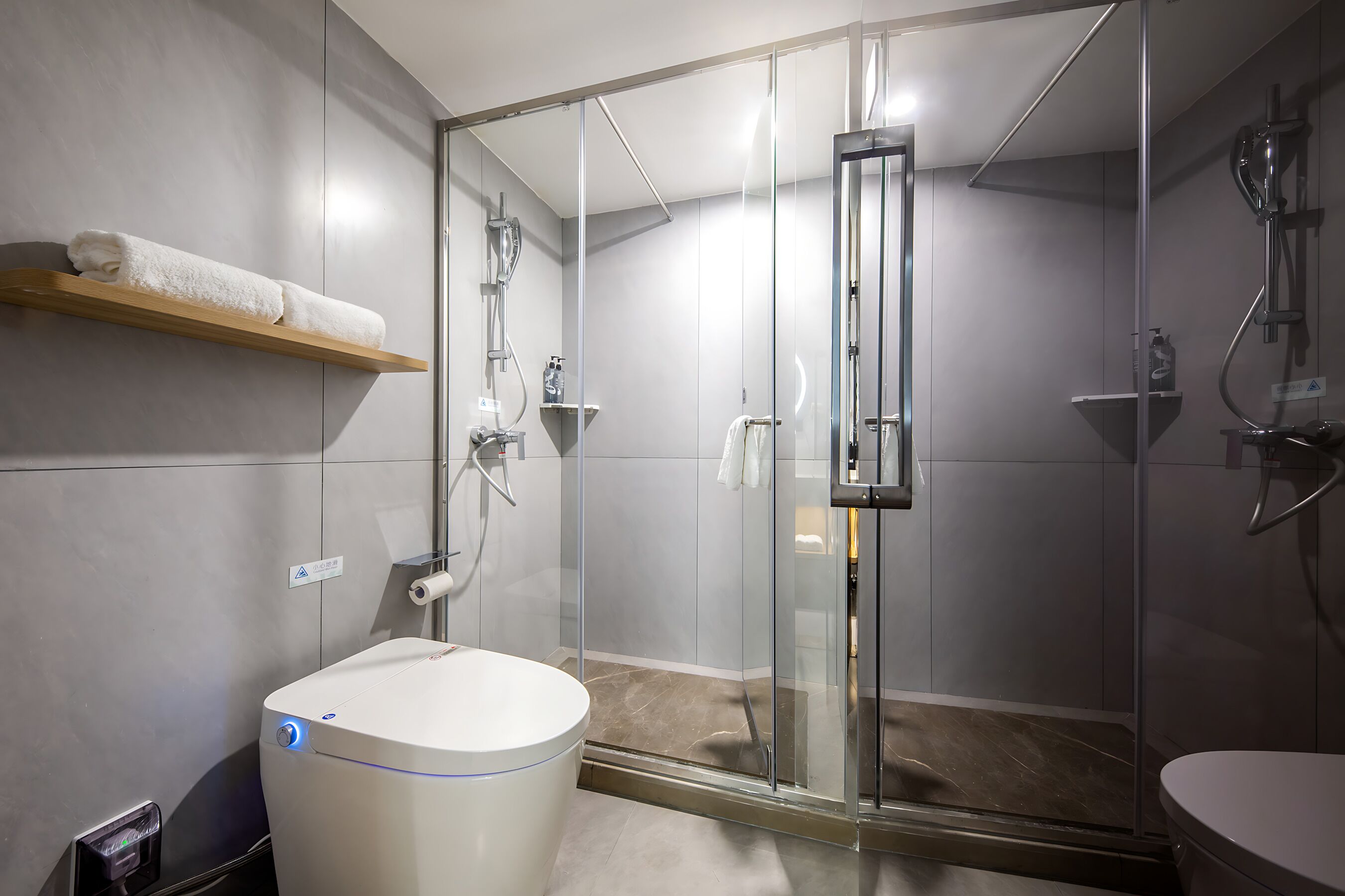 Un baño moderno con ducha de vidrio, un lavamanos blanco y un perchero.