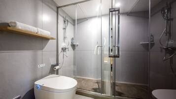 Un baño moderno con ducha de vidrio, un lavamanos blanco y un perchero.
