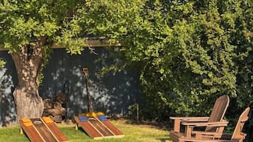 Un jardin avec une table en bois et deux chaises Adirondack, un arbre et une balançoire en bois.
