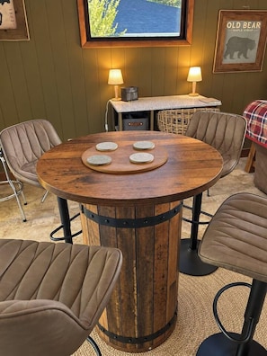 A round wooden table with a central wooden board and three circular objects, surrounded by four cushioned chairs. - 3BR Chadron home near CSC + fire pit (Chadron)