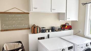 A laundry room with two white LG front-loading washers, a small trash bin, and a laundry cart.