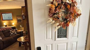 Una puerta blanca con un adorno de guirnalda, una sala de estar con un sofá, una mesa de centro y una lámpara.