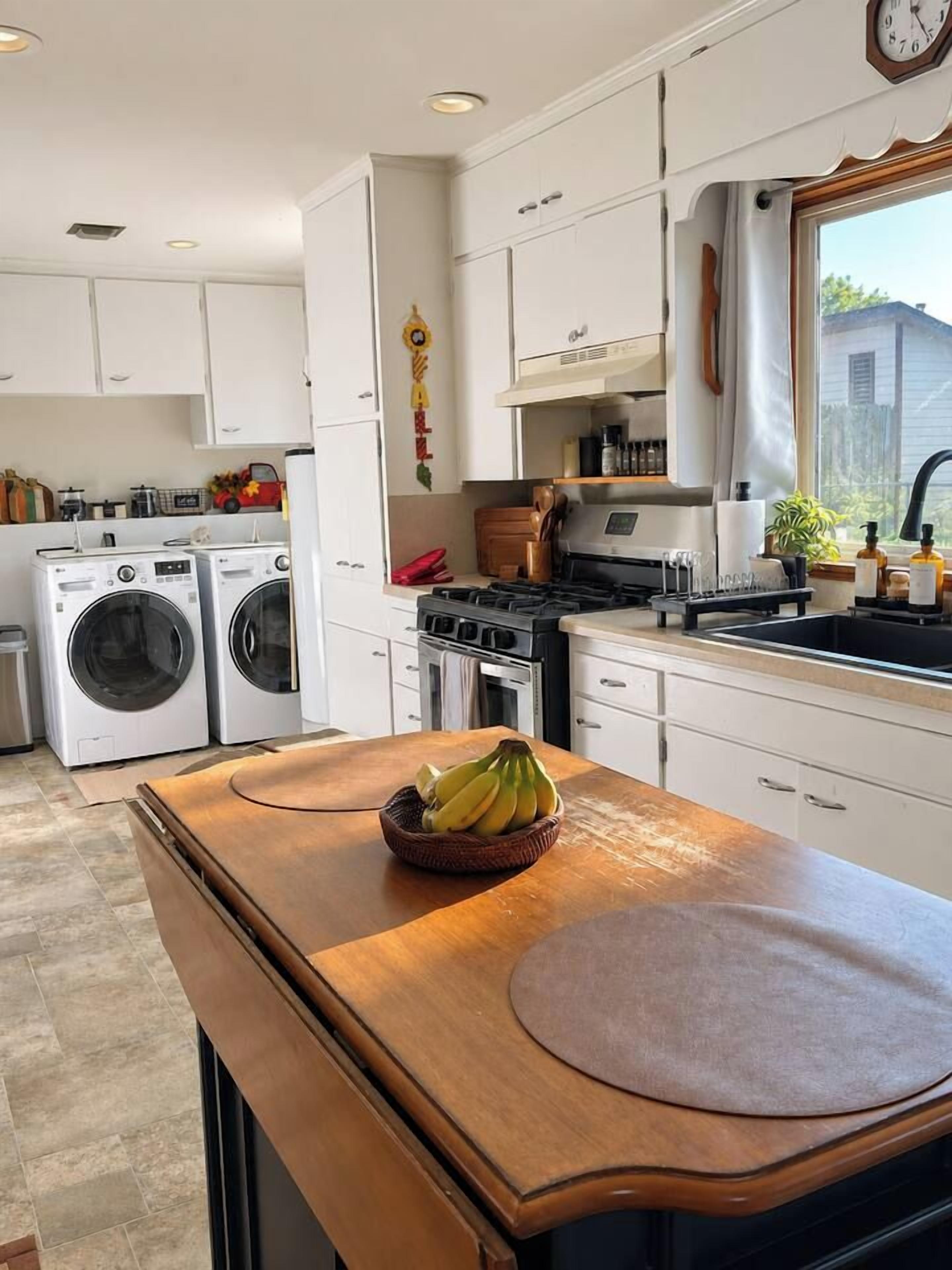 Une cuisine de taille réduite, avec des meubles blancs, une cuisinière, un évier et un lave-linge.