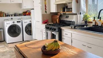 Une cuisine de taille réduite, avec des meubles blancs, une cuisinière, un évier et un lave-linge.