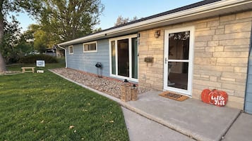 Une maison avec une façade en pierre, une porte d’entrée et un petit jardin devant, agrémenté d’un banc et d’une pancarte de bienvenue.
