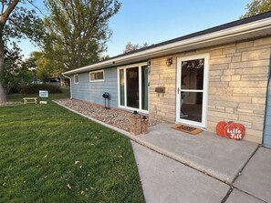 A house with a stone facade, a front door, and a small front yard with a bench and a welcome sign. - 3BR Chadron home near CSC + fire pit (Chadron)