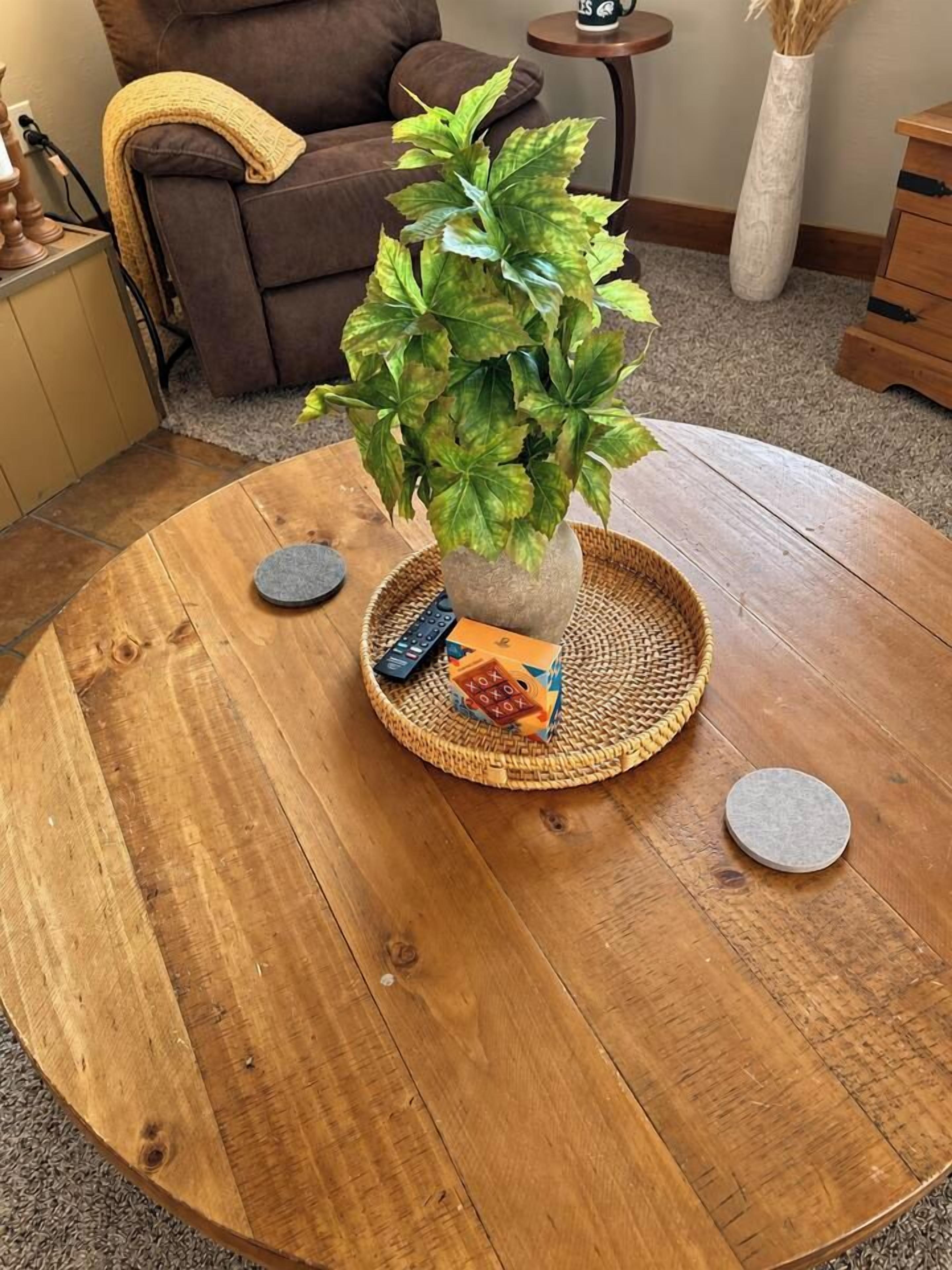 Ein runder Holztisch mit einer gewebten Tischmatte, einem Blumentopf, einer Fernbedienung und einem kleinen Dekoelement.